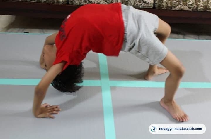 A young boy holding a bridge on a gymnastics mat