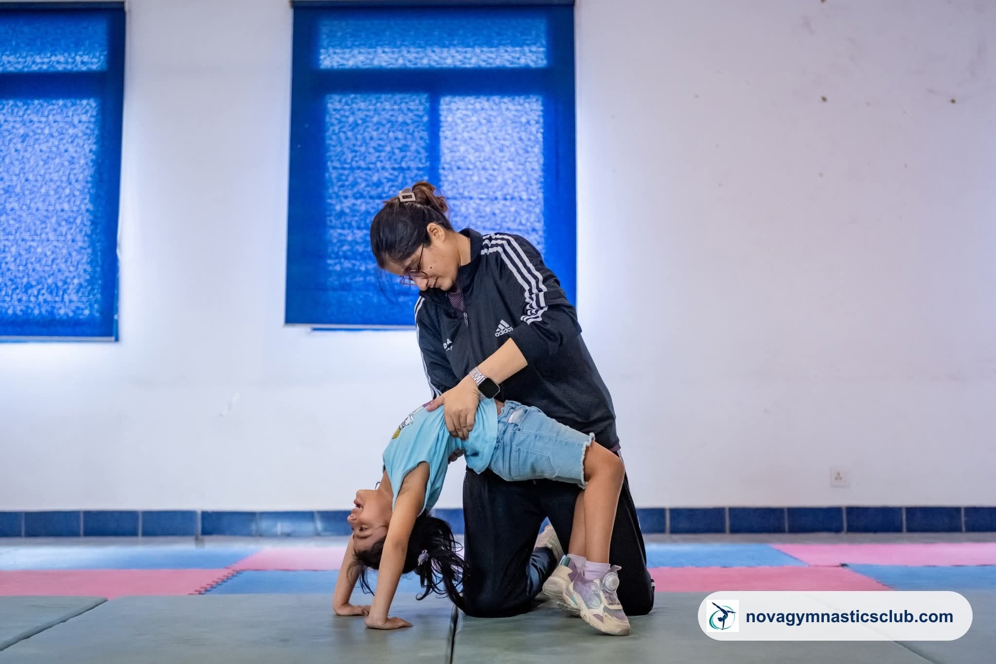 A Nova coach supporting a young girl through a backbend on the training mat