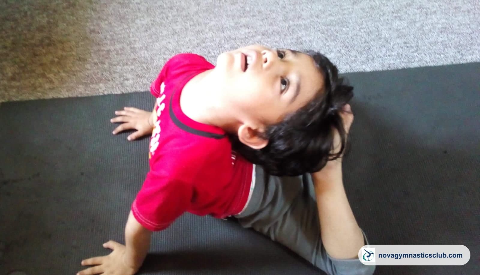 A young boy doing a back stretch on a mat
